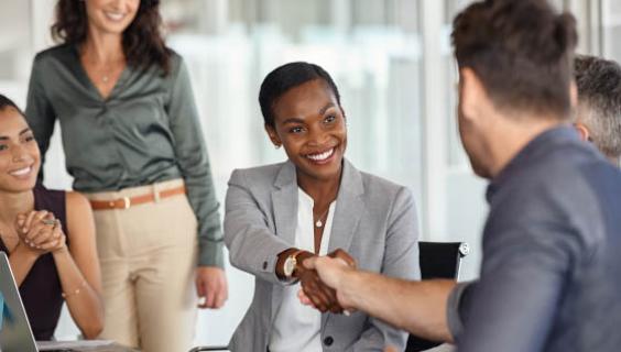 Colleagues, man and woman, shake hands as two women look on smiling